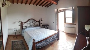 Un dormitorio con cama, una mesita, una silla, un armario y una ventana.