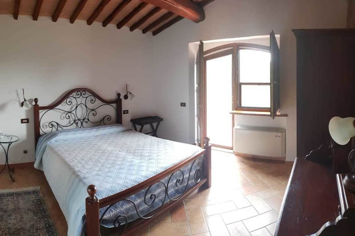 A bedroom with a bed, a small table, a chair, a wardrobe, and a window.