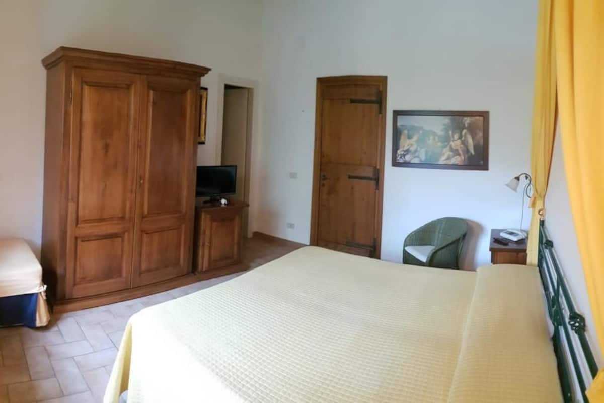 A bedroom with a bed, a wooden wardrobe, a desk with a computer, and a chair.