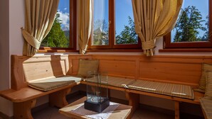 A wooden bench with cushions and a glass table, positioned by a window with curtains.