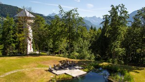 A lakeside deck with outdoor seating, surrounded by a forest and mountains in the background.