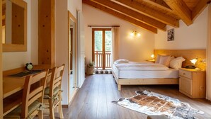 A cozy bedroom with a wooden ceiling, a large bed, bedside tables, and a desk with chairs.