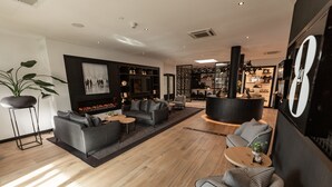 A modern living room with a sofa, armchairs, and a coffee table. There is a fireplace, a large mirror, and a bookshelf. - Gr8 Hotel Bodegraven (Bodegraven)