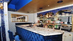 A bar area with a marble countertop, blue upholstered bar stools, and a mirrored wall. - Hotel Monte Christo (Cologne)