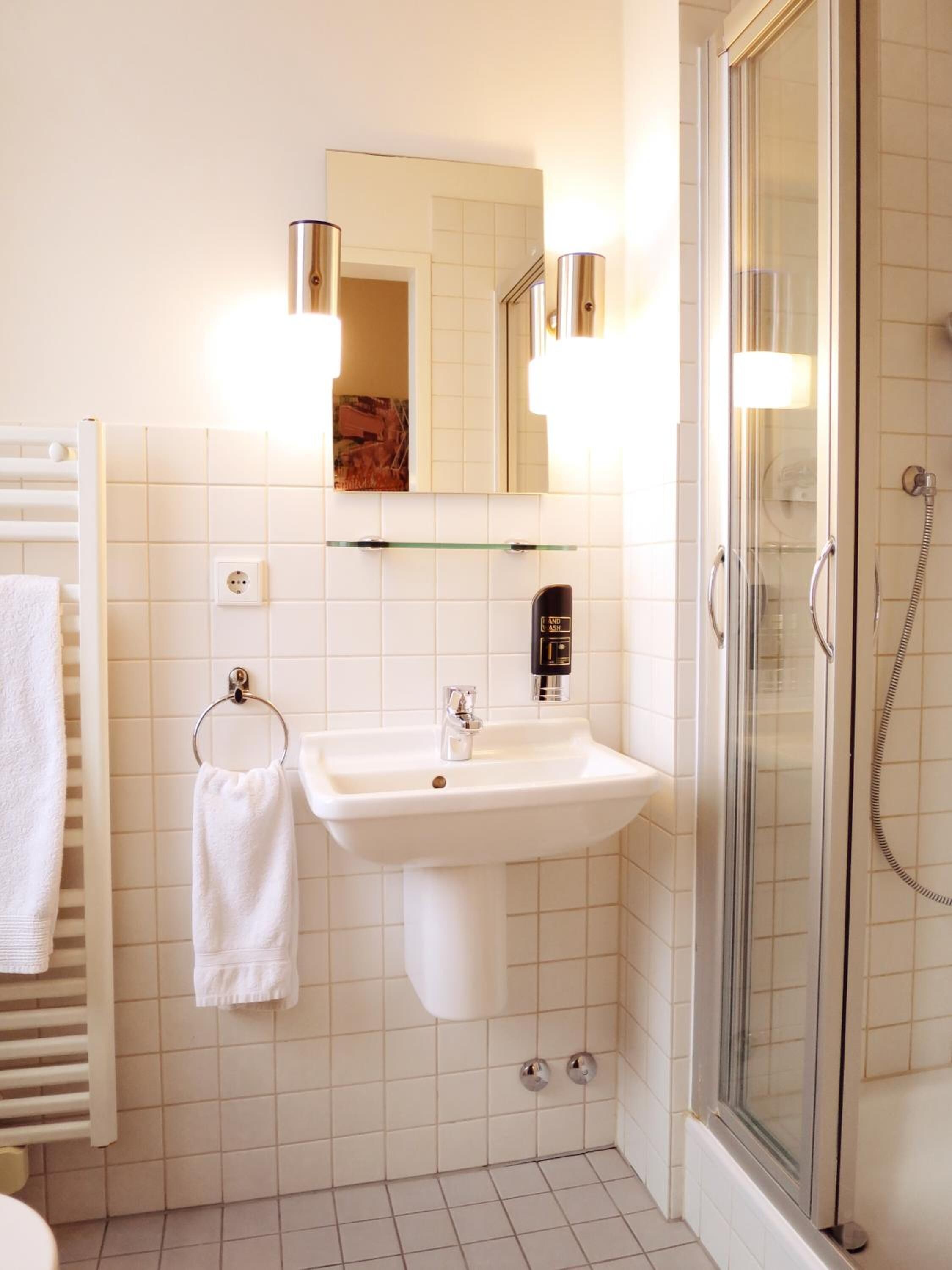 Un baño con un lavabo blanco, una cabina de ducha de vidrio y un perchero para toallas.