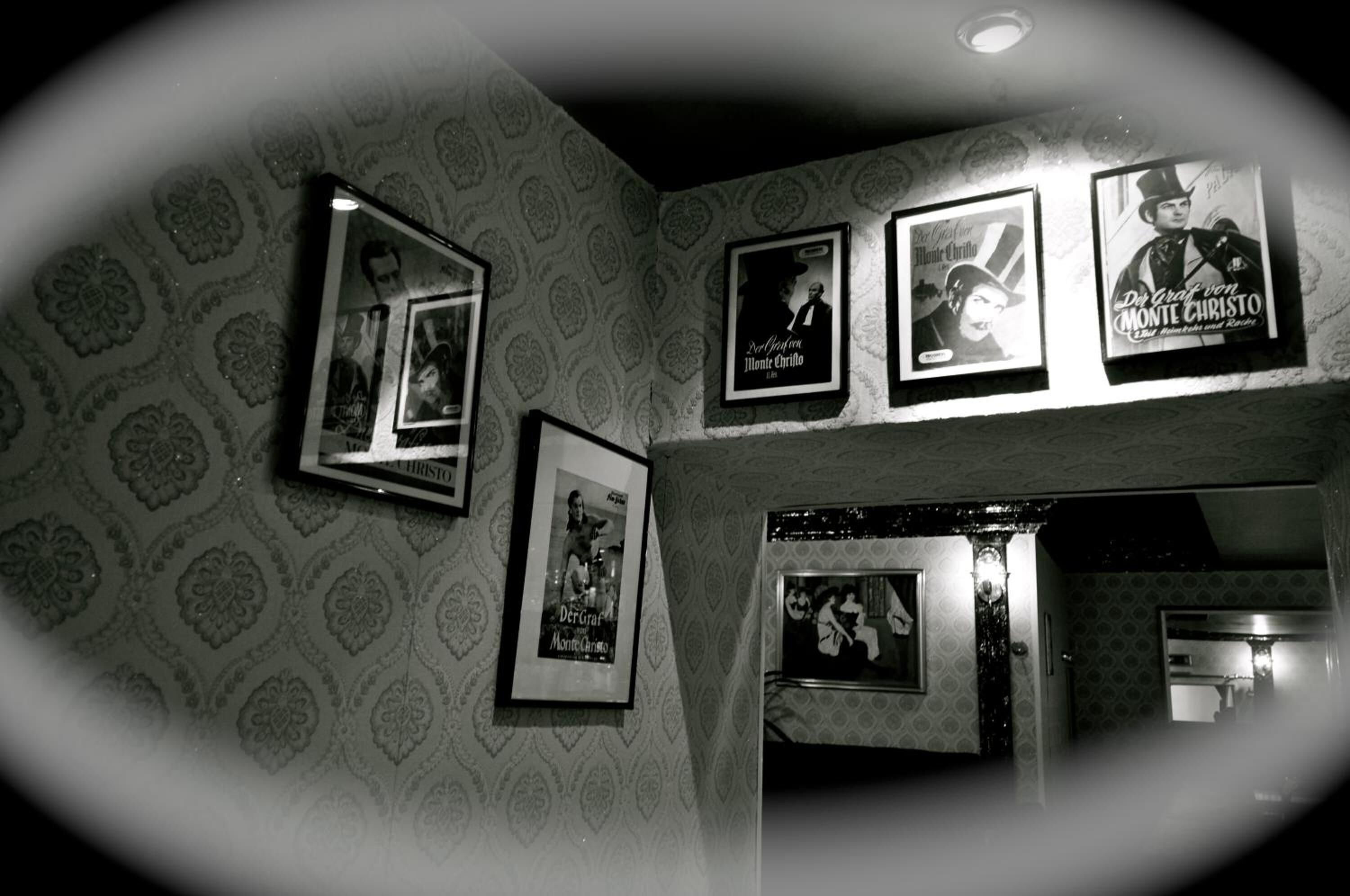 A room with patterned wallpaper, framed pictures on the wall, and a mirror reflecting part of the room.