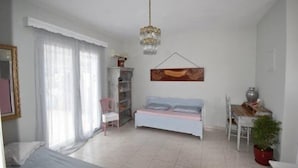 A spacious bedroom with a bed, a desk, a chair, a bookshelf, and a dining table. - Brezza Apartment D (Karpathos)