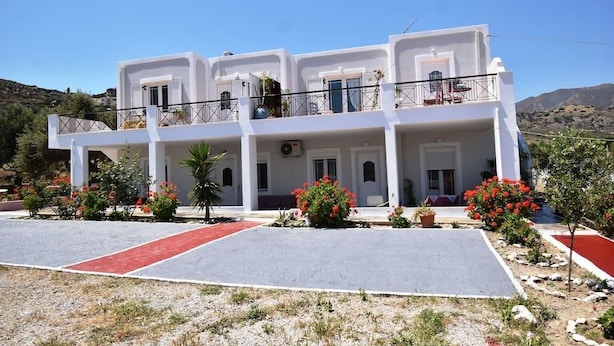 A two-story white building with balconies, a red carpet, and red flowers. - Brezza Apartment D (Karpathos)