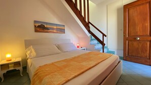 A bedroom with a bed, nightstands, a painting, a staircase, and a wooden door. - Terrazze XXV Novembre (Cefalù)