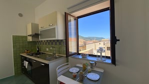 A compact kitchen with a gas stove, microwave, and a window overlooking a cityscape. - Terrazze XXV Novembre (Cefalù)