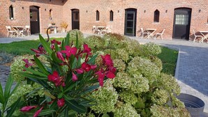 Un edificio de ladrillo con techo de tejas, mesas al aire libre y un jardín con flores.