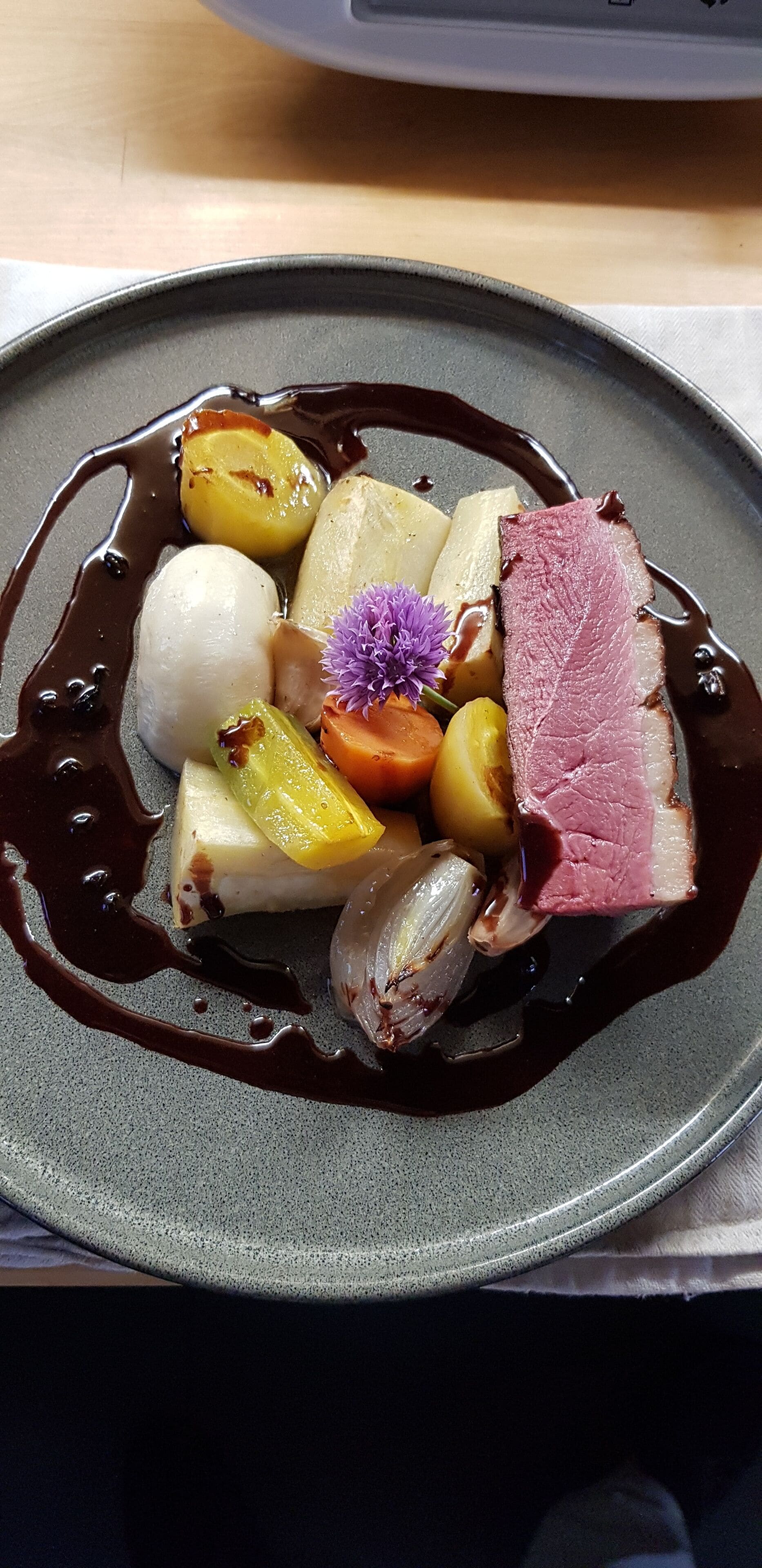 A dessert plate with various fruits, a piece of meat, and a decorative flower.