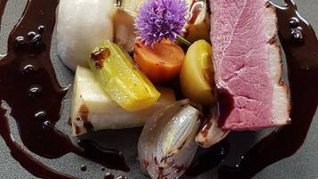 A dessert plate with various fruits, a piece of meat, and a decorative flower.