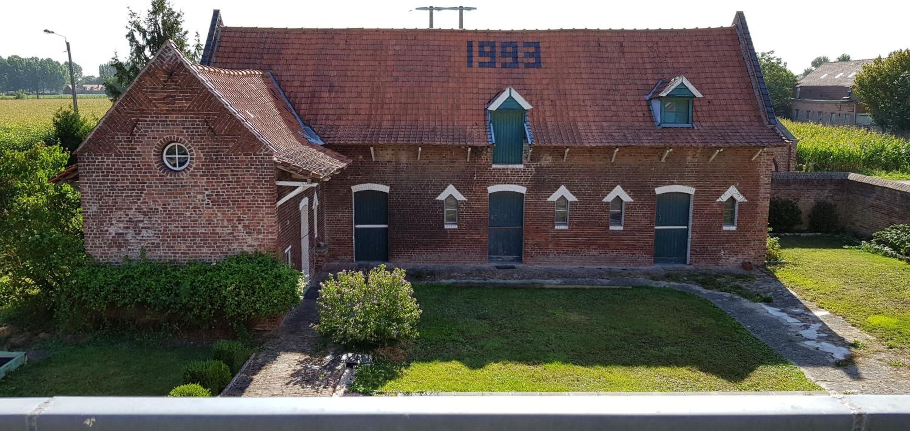 A brick building with a tiled roof, a year marked '1993', and a small garden area in front.