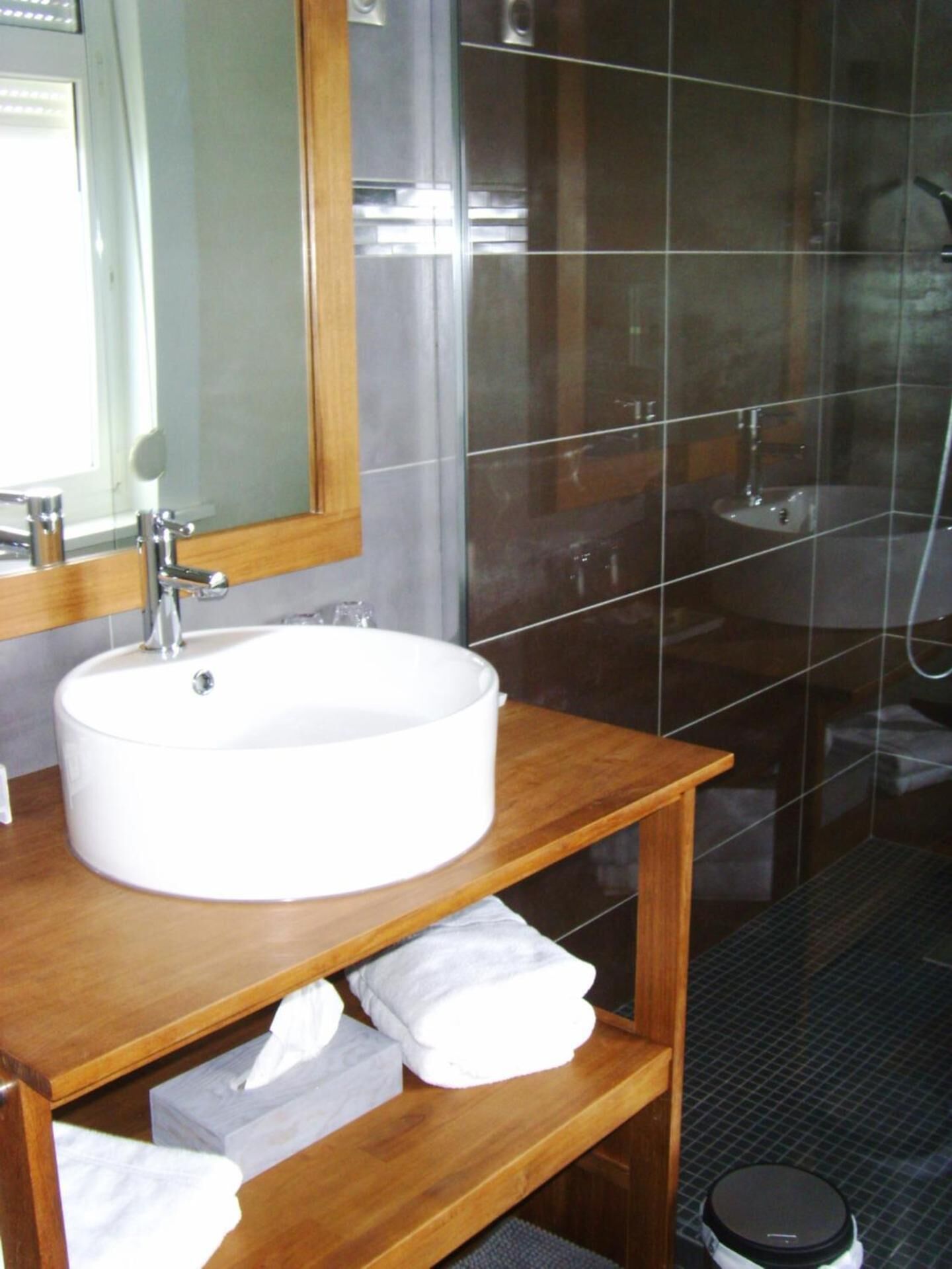 Une salle de bain avec un lavabo blanc, un meuble-lavabo en bois et une cabine de douche en verre.