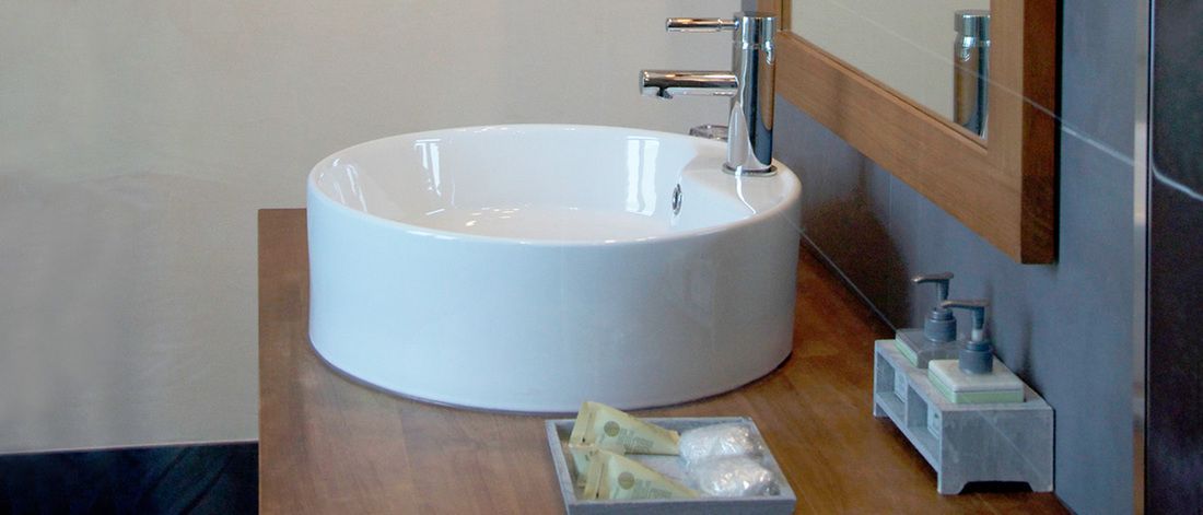 A modern bathroom with a round white sink, a wooden vanity, and a small step stool.