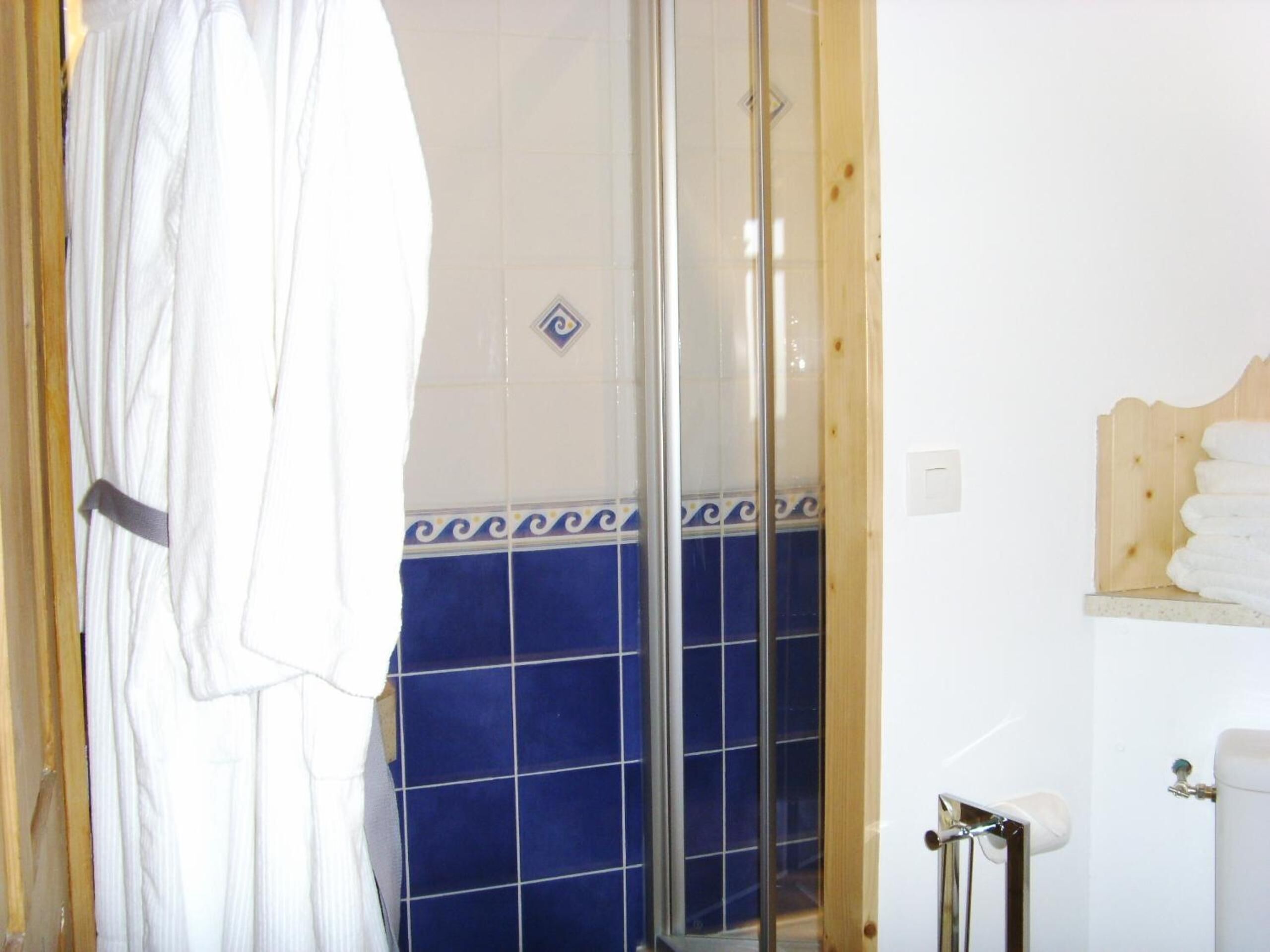 A bathroom with a glass shower enclosure, a white bathtub, and a wooden shelf with towels.