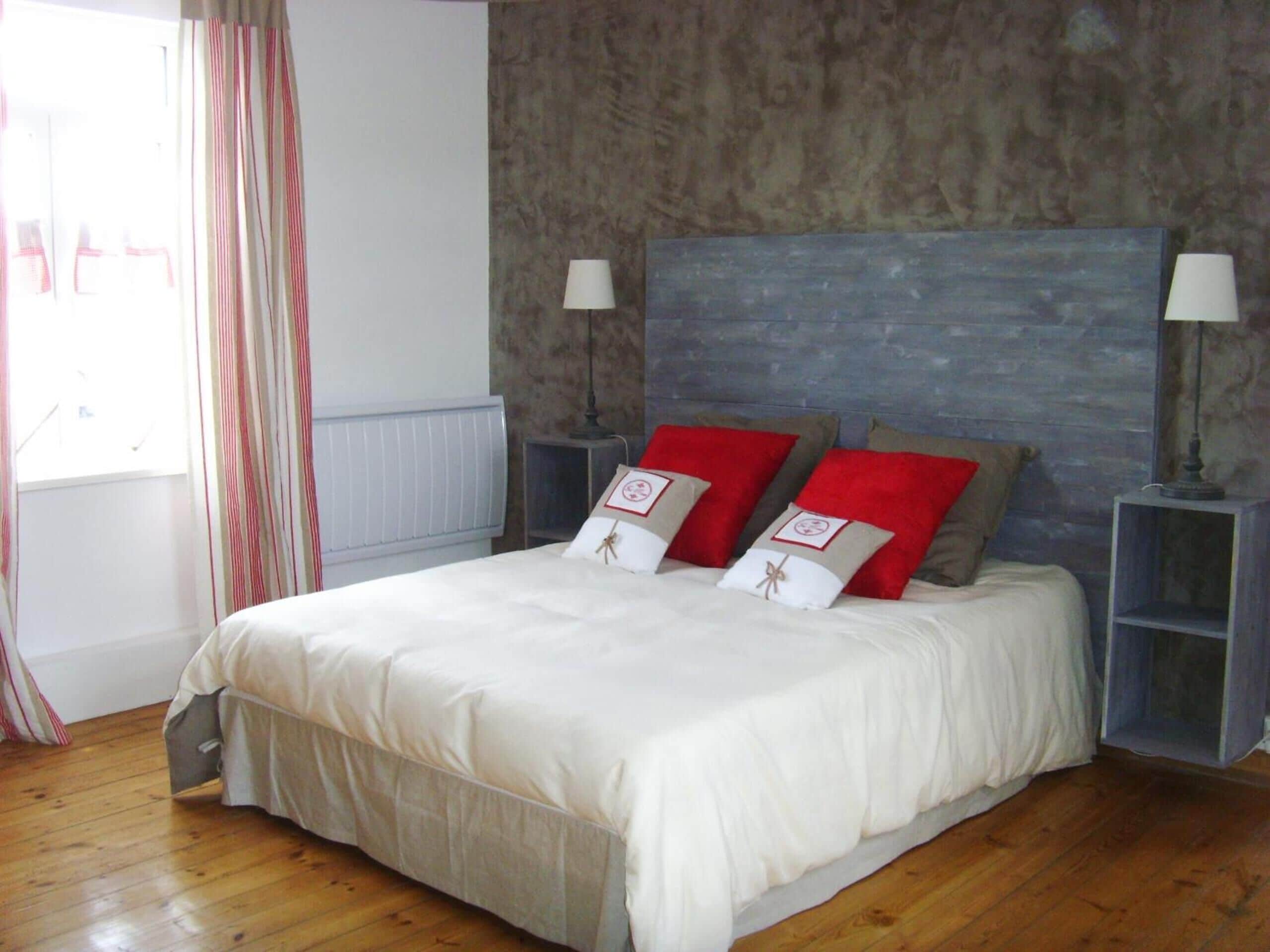 A bedroom with a large bed, two bedside tables with lamps, a radiator, and a window with curtains.