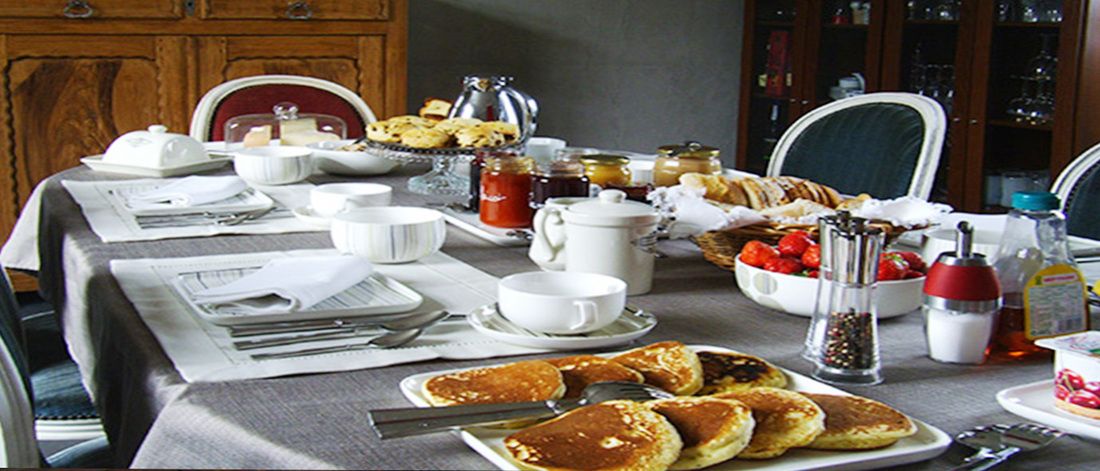 A breakfast table set with various dishes, including pancakes, pastries, and a fruit bowl.