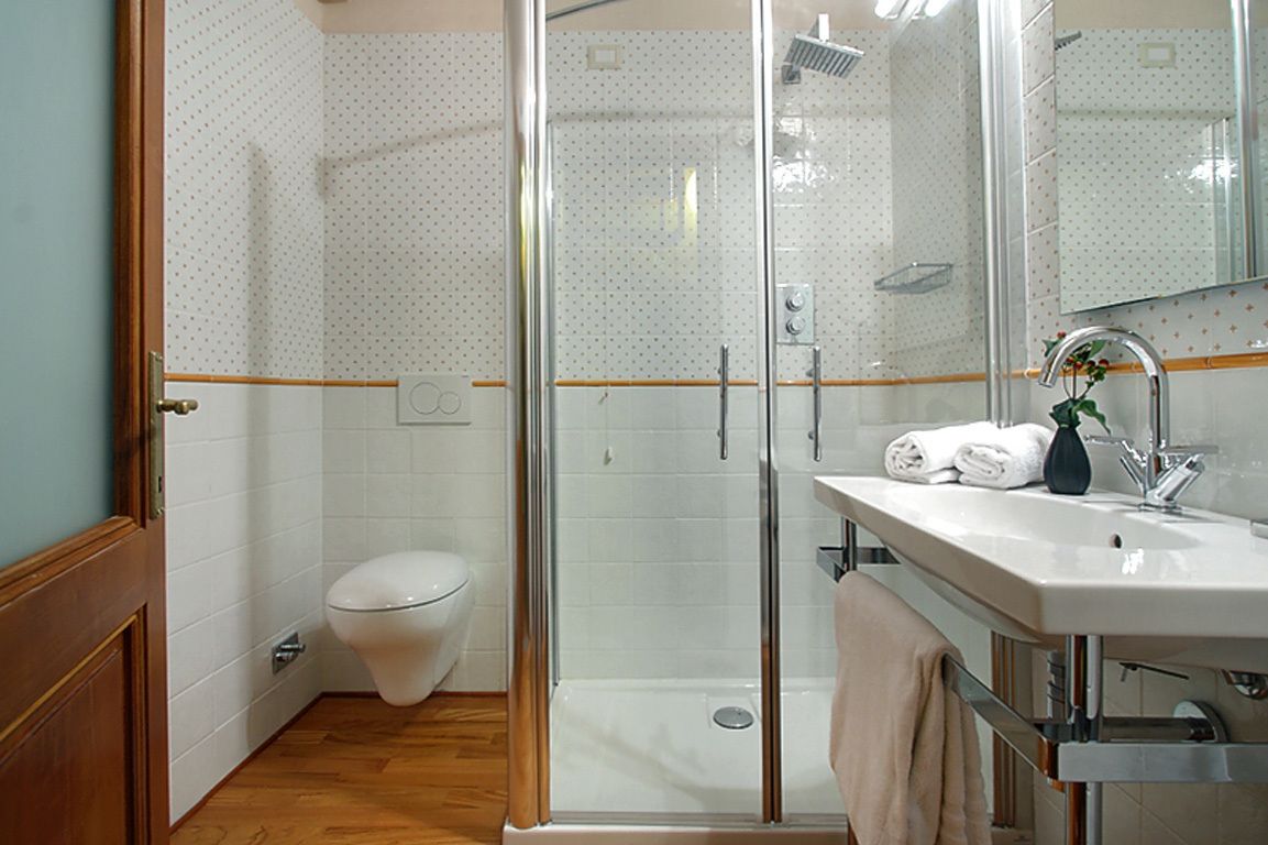 A bathroom with a glass-enclosed shower, a white toilet, and a sink with a towel and vase.