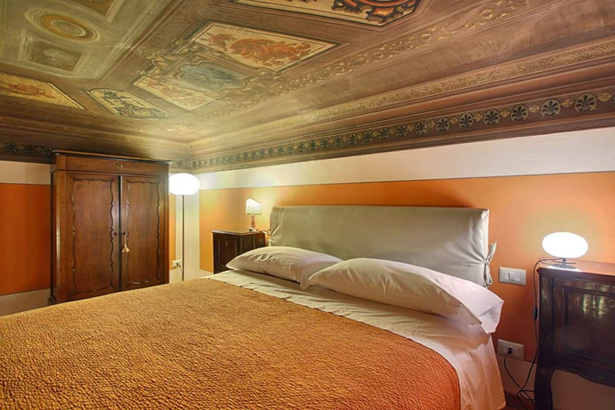 Une chambre d’hôtel avec un grand lit, une armoire en bois et un plafond orné de motifs décoratifs.