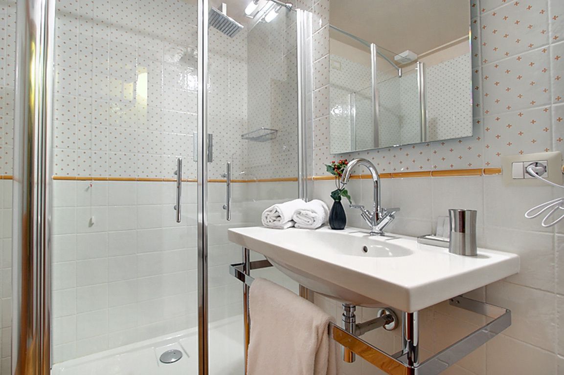 A modern bathroom with a glass shower enclosure, a white sink with a chrome faucet, and a mirror above the sink.