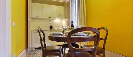 Un comedor con una mesa redonda y cuatro sillas, una cocina con armarios blancos y un suelo estampado.