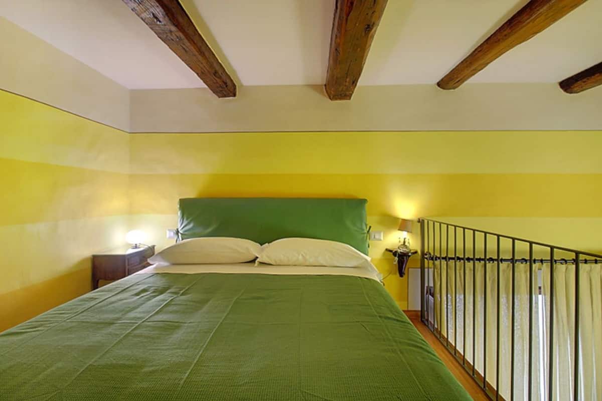 Une chambre avec une couvre-lit verte, des poutres en bois au plafond et un mur jaune.