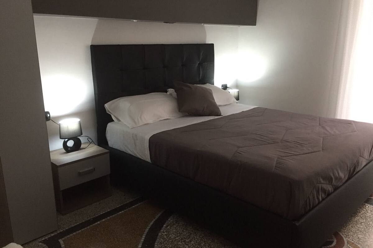 A modern hotel room with a large bed, a nightstand, and a wall-mounted TV.