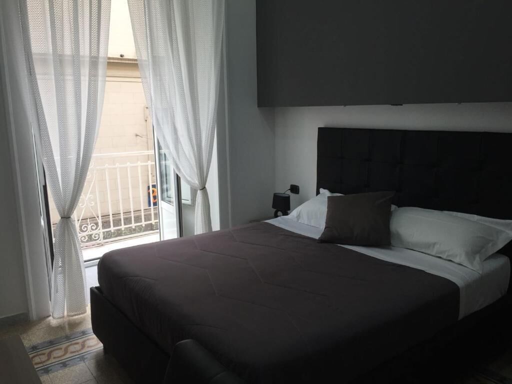A hotel room with a large bed, a headboard, a nightstand, and sheer curtains.