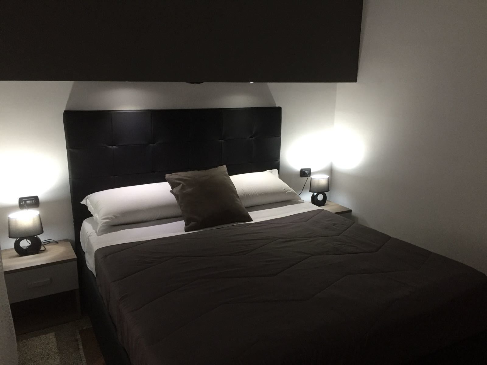 A neatly made bed with a dark quilt, two bedside lamps, and a headboard.