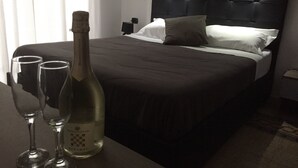 A hotel room with a large bed, a bedside table with two wine glasses and a bottle, and a nightstand with a lamp. - MB95 Mezzocannone Luxurious B&B (Naples)