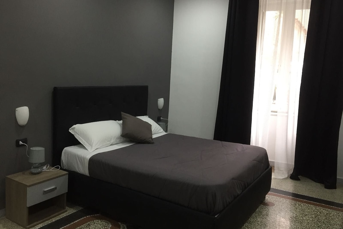 A modern bedroom with a large bed, a bedside table with a lamp, and a window with curtains.