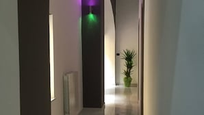 A hallway with a modern design, featuring a central column with purple and green lighting, a potted plant, and a radiator on the wall. - MB95 Mezzocannone Luxurious B&B (Naples)