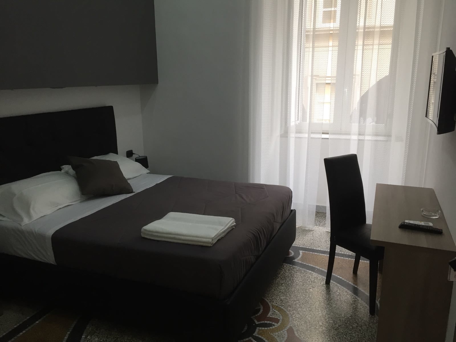 A hotel room with a bed, a desk, a chair, and a TV on the wall.