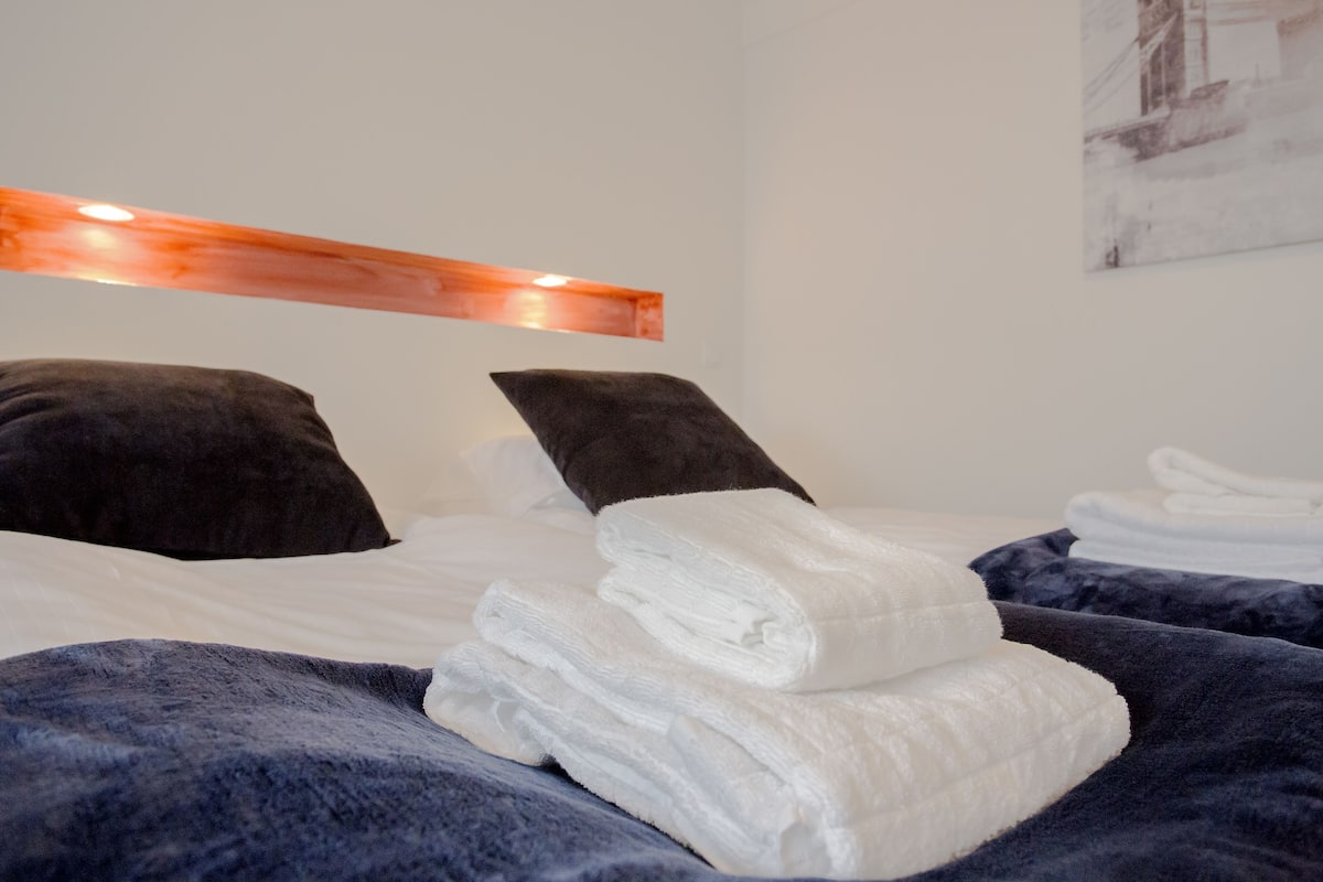 A neatly made bed with white linens and a folded towel on a dark blue blanket.