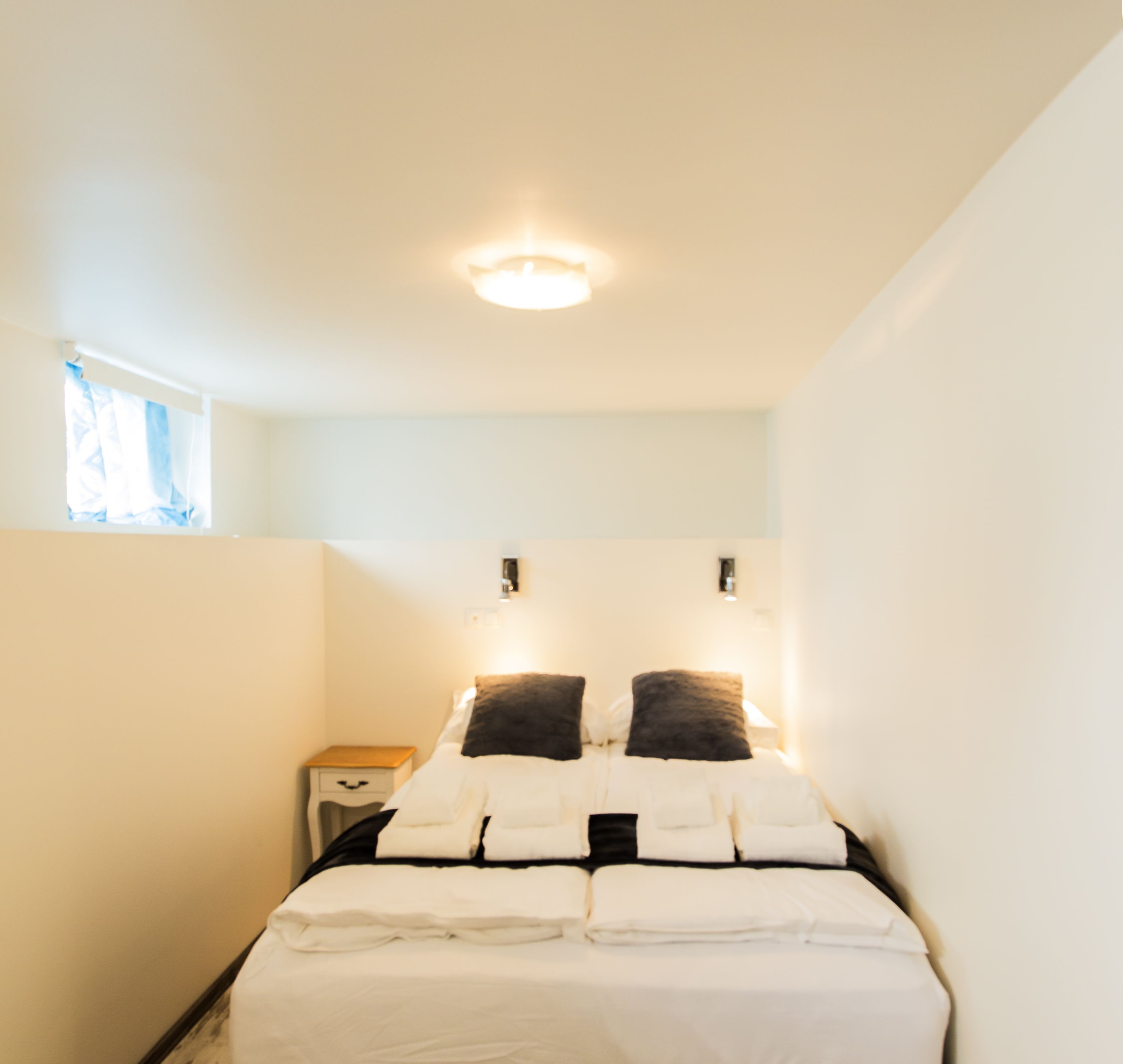 A small, neatly arranged bedroom with a single bed, a nightstand, and a window with curtains.