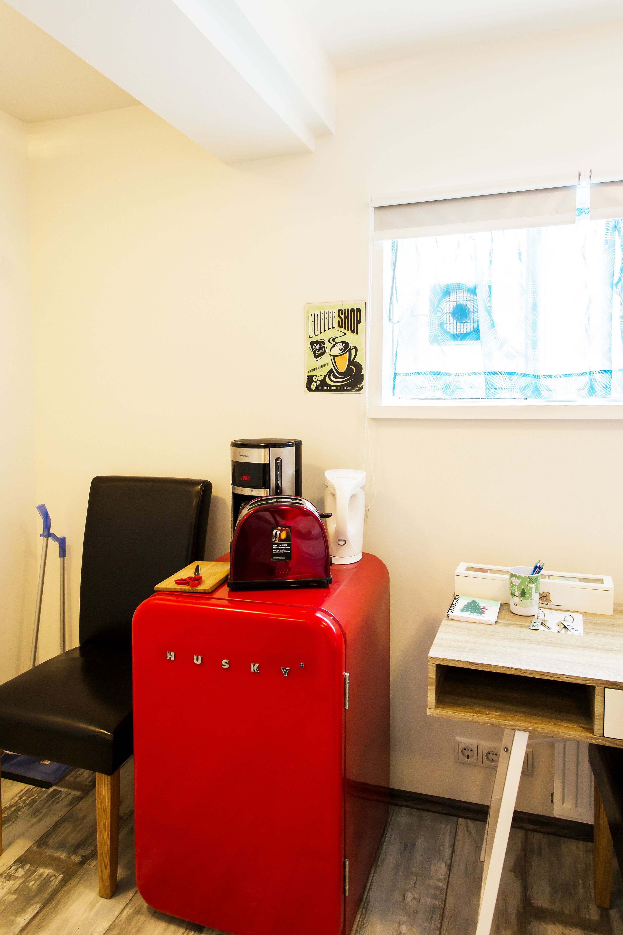 Una habitación compacta con una silla roja, una cafetera y una mesita con una taza y un cuaderno.