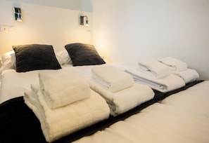 A neatly made bed with white and brown pillows, folded white towels, and a black headboard.