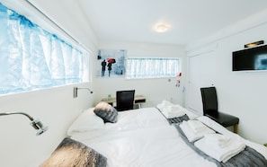 A hotel room with a bed, a desk, a chair, a TV, and a window with curtains.