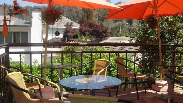 Una terraza con sillas de mimbre, una mesa de vidrio y sombrillas naranjas.
