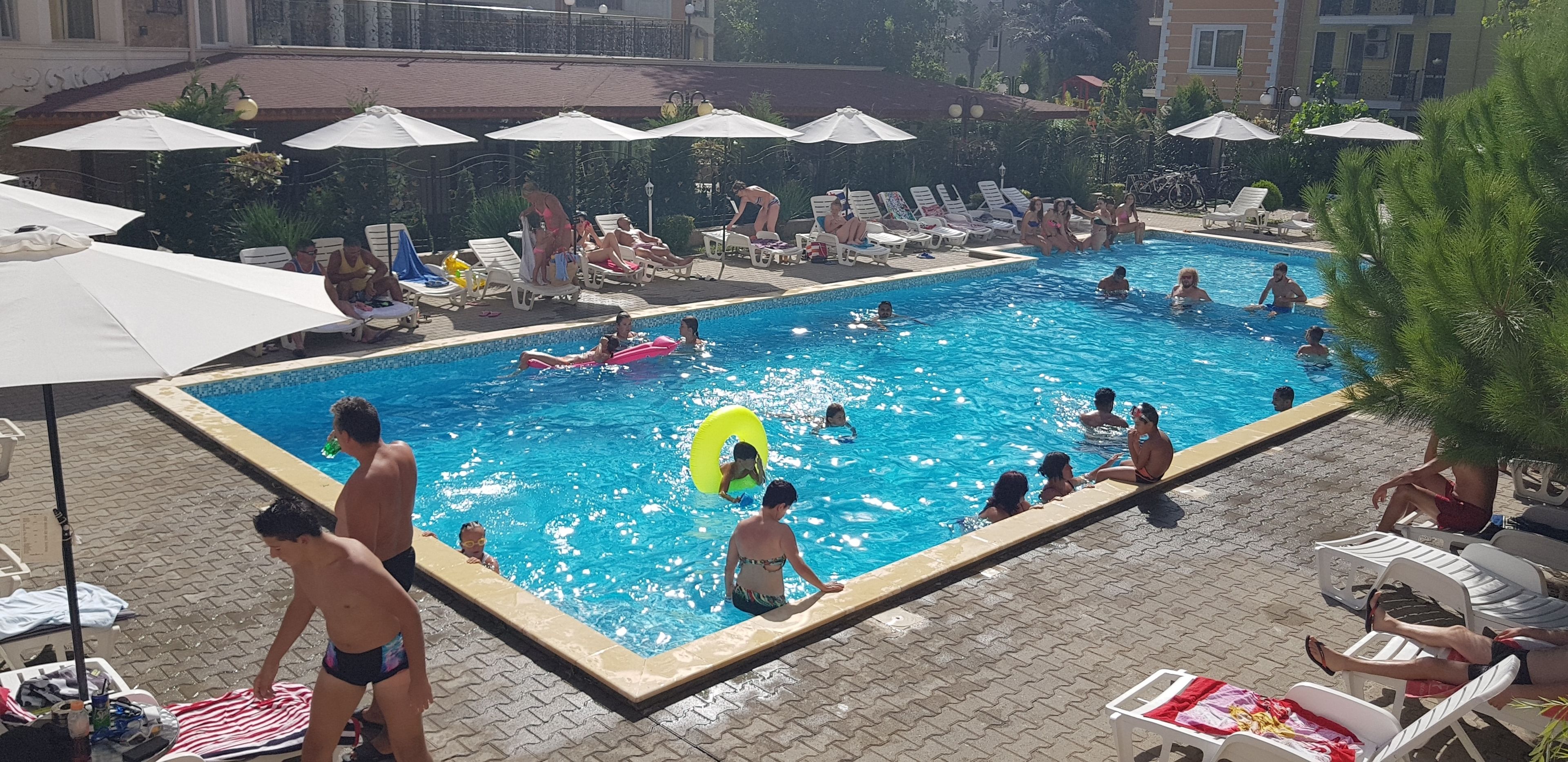 A swimming pool with lounge chairs and umbrellas, surrounded by buildings.