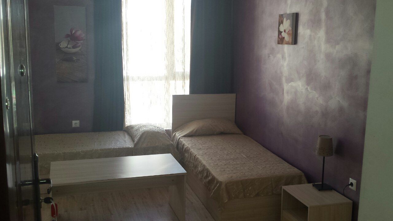 Un dormitorio con dos camas, una mesita de noche, una lámpara y un ventanal con cortinas.
