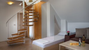 Ein modernes Interieur mit einer Wendeltreppe aus Holz, einem Schlafsofa, einem kleinen Tisch mit einer Flasche und einer Kiste sowie einer Blumenvase.