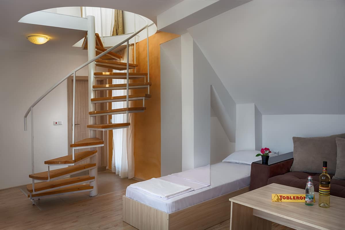 Un intérieur moderne avec un escalier en colimaçon en bois, un canapé-lit, une petite table avec une bouteille et une boîte, et un vase à fleurs.