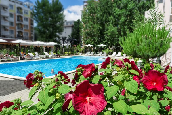 Ein Swimmingpool mit Liegestühlen und Sonnenschirmen, umgeben von roten Blumen und Grünpflanzen.
