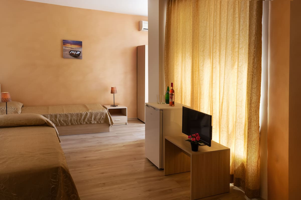 Une chambre d’hôtel comprenant un lit, un bureau avec une télévision, un petit réfrigérateur, une table de chevet avec une lampe et une fenêtre avec des rideaux.