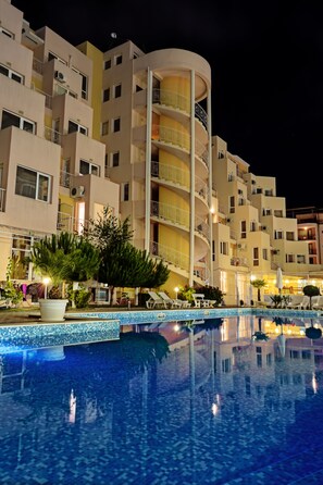 Ein mehrstöckiges Hotel mit Schwimmbad, Außenbereich und gut beleuchteter Fassade.