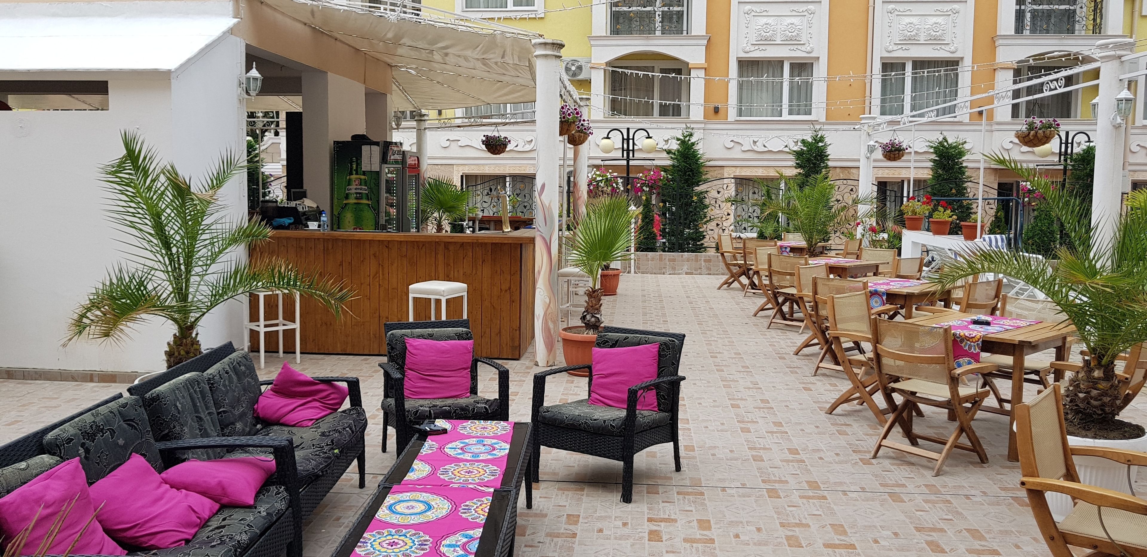 An indoor courtyard with outdoor seating, including sofas and chairs, surrounded by potted plants and a central bar area.