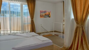 Ein Hotelzimmer mit zwei Betten, einem Fenster mit durchsichtigen Vorhängen, einem Bild an der Wand und einem weißen Geländer in der Nähe des Fensters.